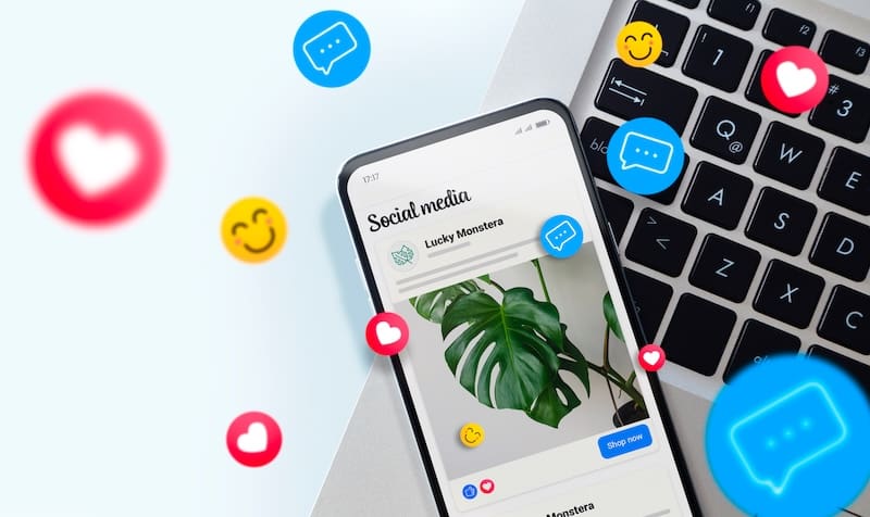 Social Media ads on mobile phone screen. Smartphone and over laptop keyboard showing advertising example in a social network. Many emojis around it.