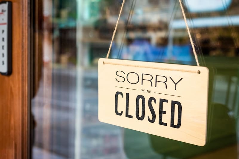 A wooden sign hanging on a glass door reads “SORRY WE ARE CLOSED.” The background is slightly blurred, as if someone might need to delete Google business hours for this location.