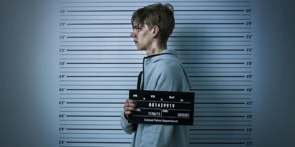 a young man holding a sign in front of a mugshot mug.