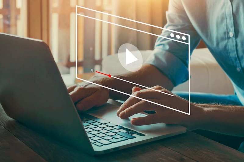 A person types on a laptop with an overlay image of a video playback interface, including a play button and progress bar, suggesting they are either watching or editing a "how to get Google reviews" tutorial. Sunlight streams through a window in the background.