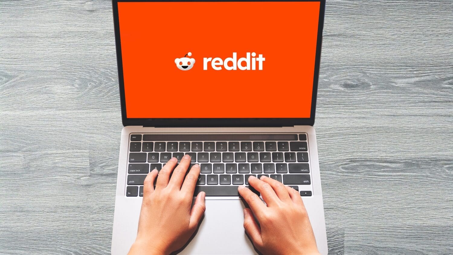 A person's hands on the keyboards of a laptop with Reddit on the screen.